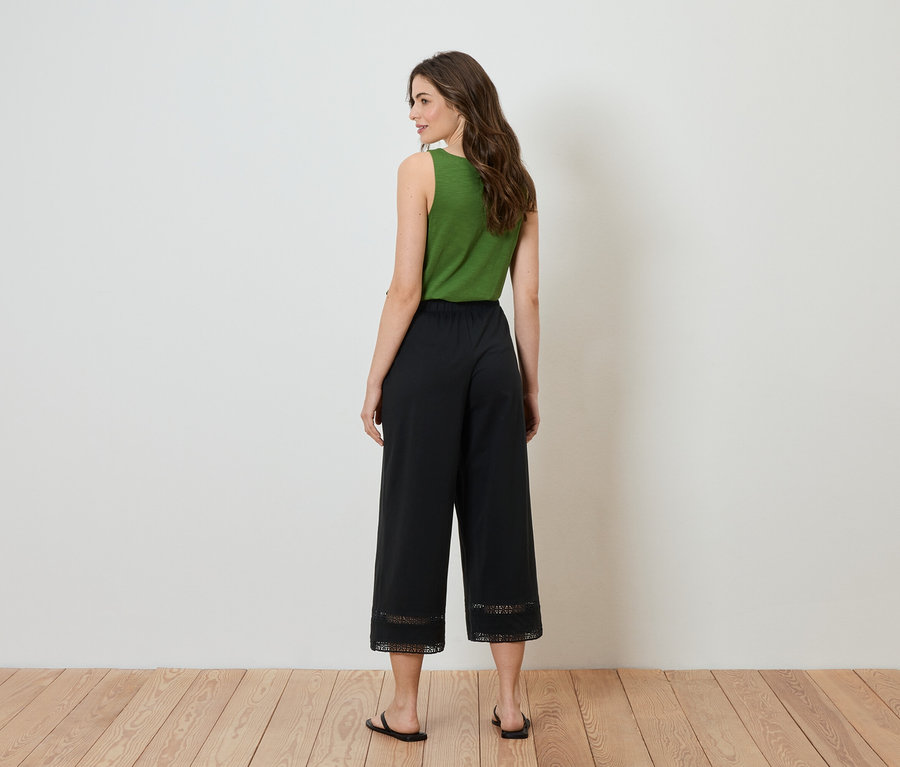 Une femme se tient dos à la caméra, elle porte un haut vert et une culotte noire avec de la dentelle en bas.