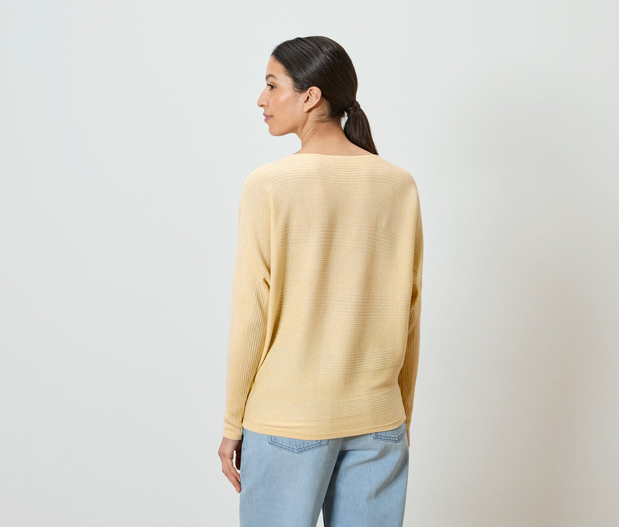Une femme avec une queue de cheval porte un pull jaune et un jean bleu clair.