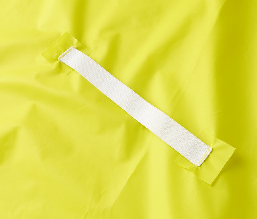 Gros plan d'un tissu jaune avec un élastique blanc fixé à deux morceaux de tissu jaune.