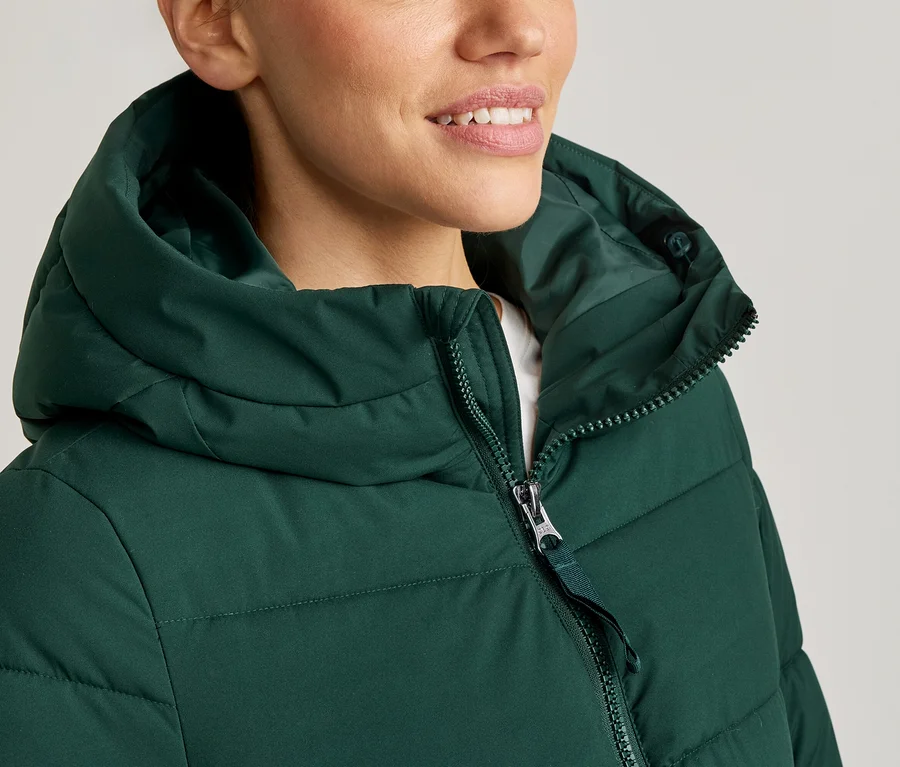 Femme portant un manteau à capuche vert, fermeture éclair à moitié fermée.