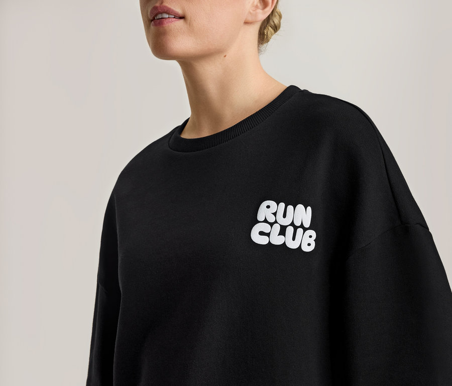 Femme portant un sweatshirt noir avec l'inscription blanche "RUN CLUB".
