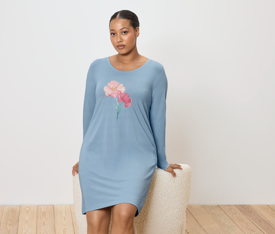 Femme assise sur un tabouret, portant une chemise de nuit bleue avec un motif floral.