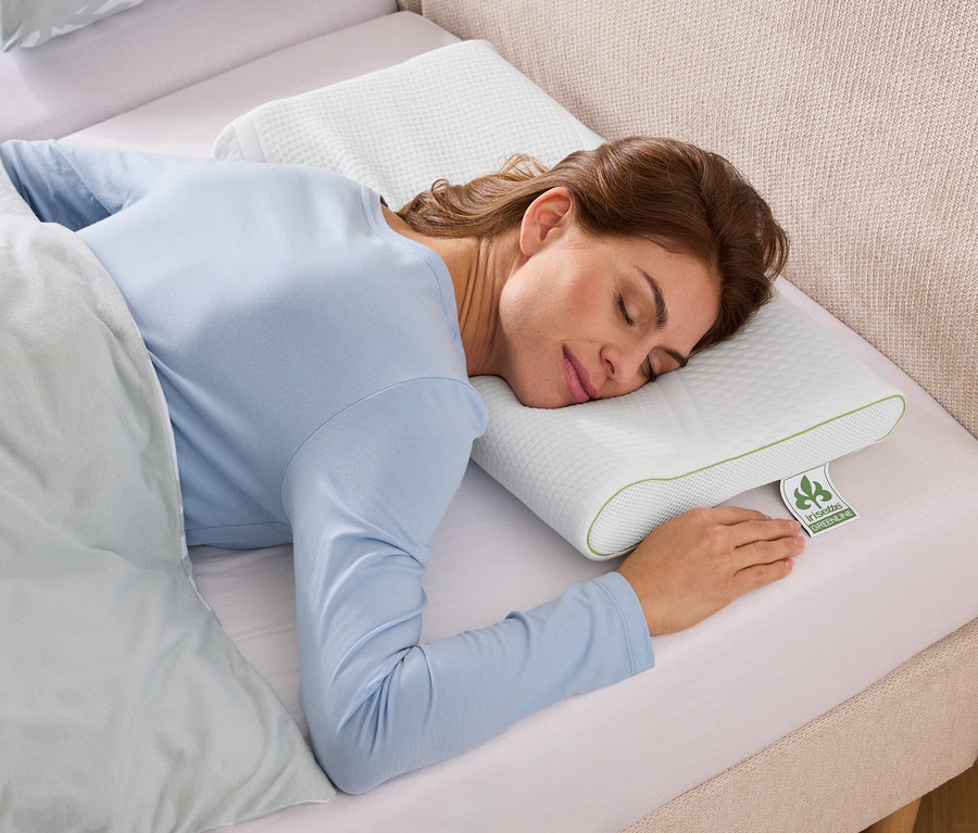 Une femme dort sur un oreiller blanc texturé avec des accents verts dans un lit avec des draps bleu clair.