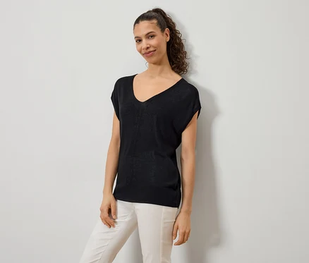 Une femme porte un haut noir à col en V et un pantalon de couleur claire.