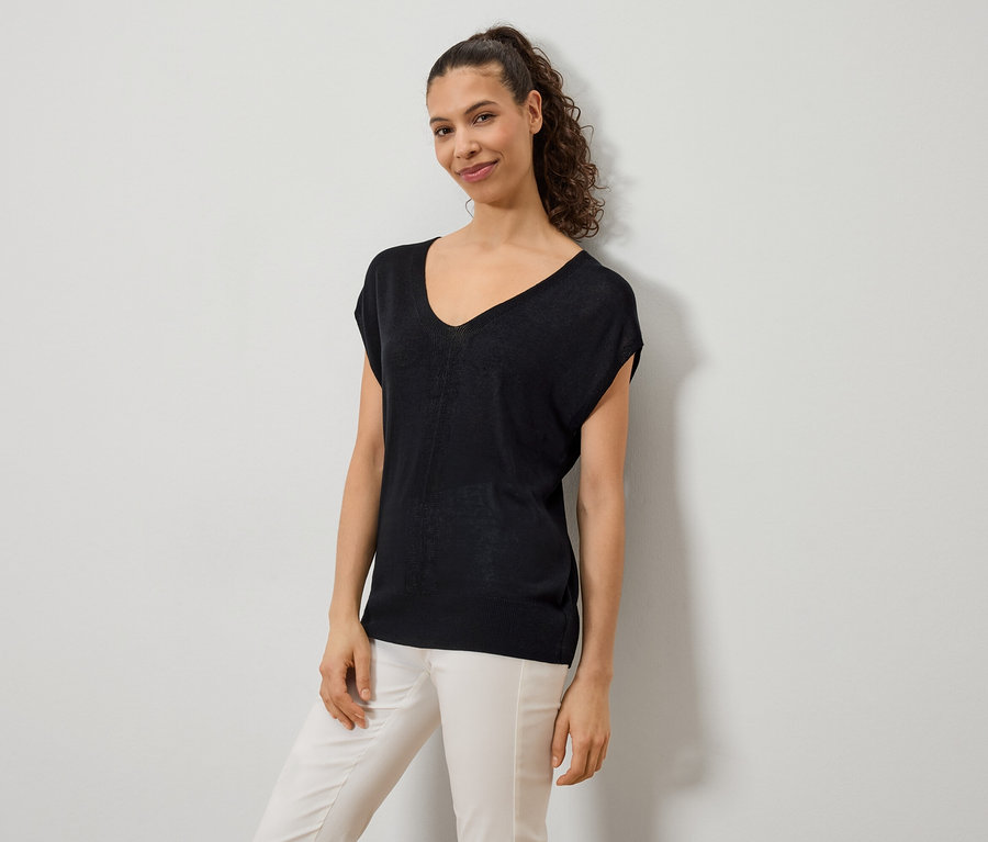Une femme porte un haut noir à col en V et un pantalon de couleur claire.