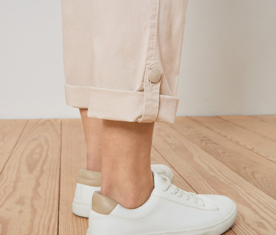 Gros plan d'une personne portant un pantalon beige boutonné et des baskets blanches.