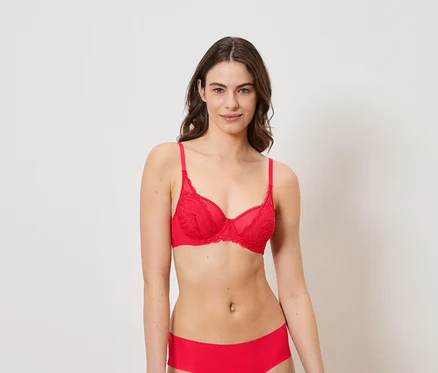 Une femme aux cheveux bruns porte un soutien-gorge rouge en dentelle et une culotte rouge sur fond blanc.