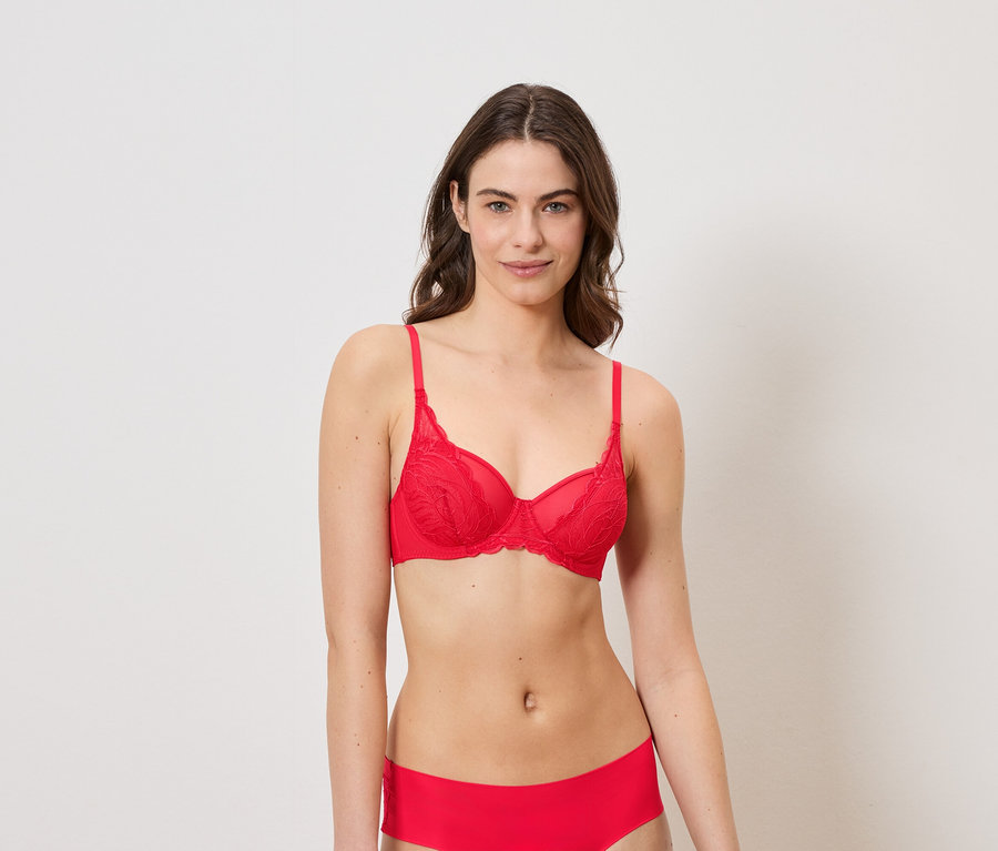Une femme aux cheveux bruns porte un soutien-gorge rouge en dentelle et une culotte rouge sur fond blanc.
