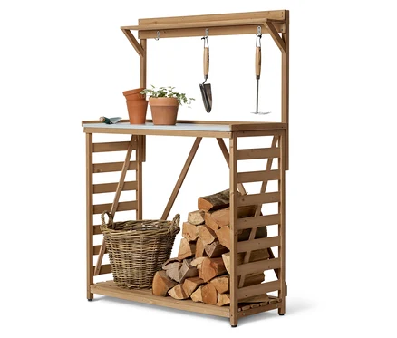 Une table de jardin en bois avec des plantes, des pots, des outils, un panier et des bûches.