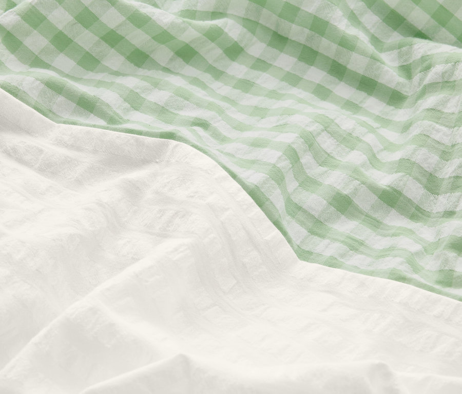 Gros plan de linge de lit froissé : une partie est blanche, l'autre à carreaux verts et blancs.