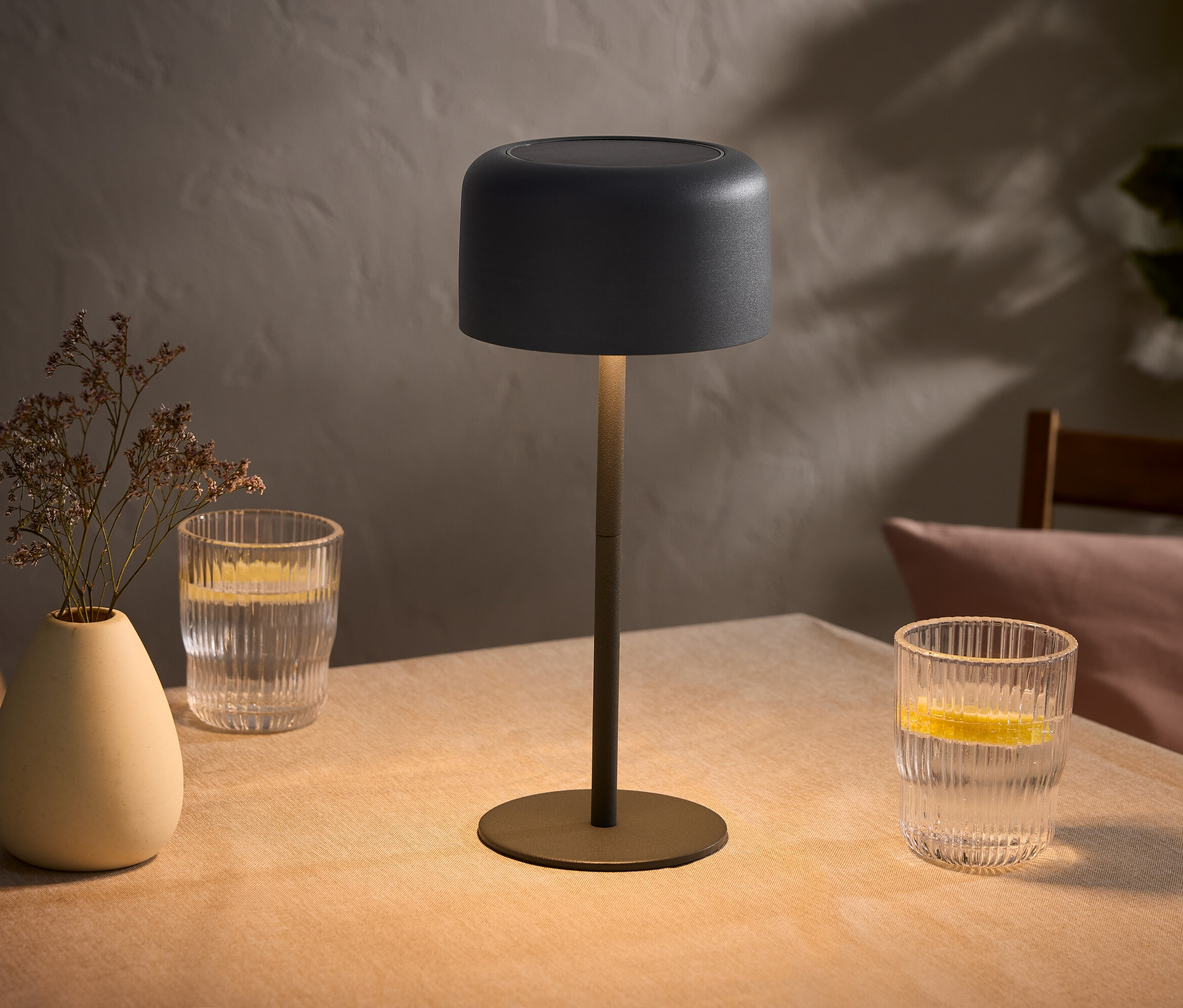 Table avec lampe, vase avec des fleurs et deux verres d'eau avec du citron.