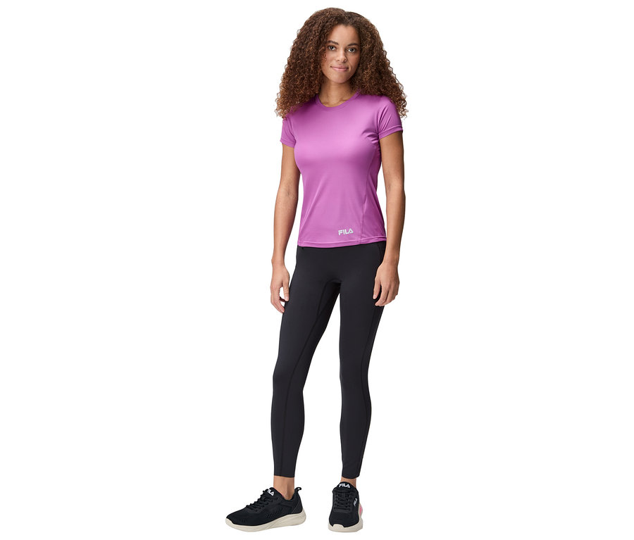 Femme debout portant un t-shirt Fila violet, un legging noir et des baskets noires.
