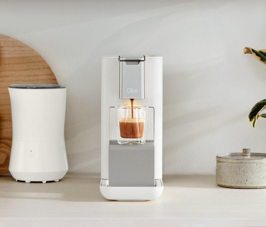 Sur un comptoir de cuisine se trouvent les machines à café Qbo ESSENTIAL Bright Sand et Qbo ICONIC Dark Chrome.