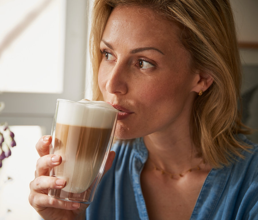 Femme buvant un latte macchiato dans un verre à double paroi.