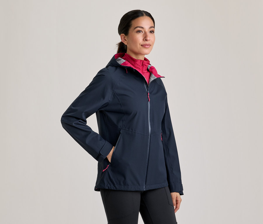 Femme portant une veste bleu marine avec une doublure rose et un pantalon noir, la main dans la poche.