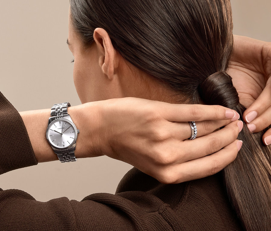 Une femme attache ses cheveux en queue de cheval, elle porte une montre argentée et une bague.