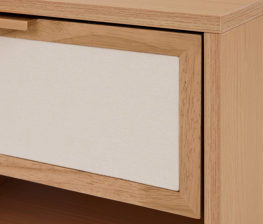 Gros plan d'un tiroir en bois clair avec un panneau frontal en tissu crème et une petite poignée en bois.
