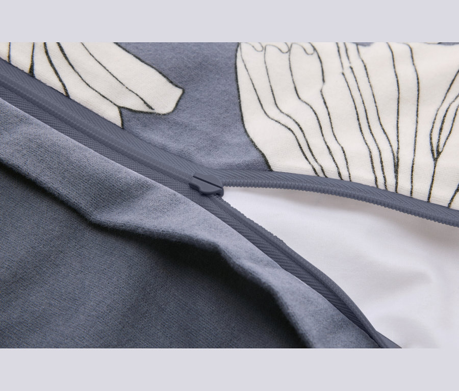 Gros plan d'un tissu gris avec une fermeture éclair partiellement ouverte, révélant un tissu blanc en dessous. Le tissu gris présente un motif blanc avec des contours noirs.