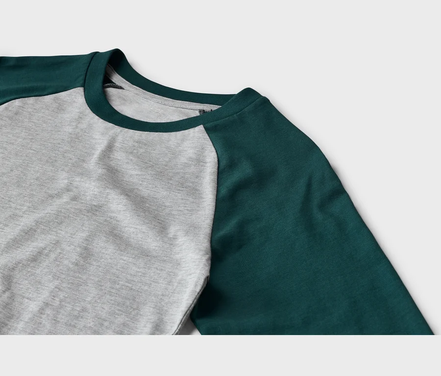 Gros plan d'un t-shirt à manches longues avec un corps gris et des manches raglan vert foncé, doté d'un col rond vert foncé.