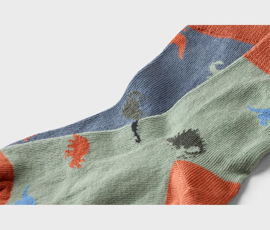 Gros plan de deux paires de chaussettes dans les tons vert et bleu avec un motif de dinosaures et des pointes et talons orange.