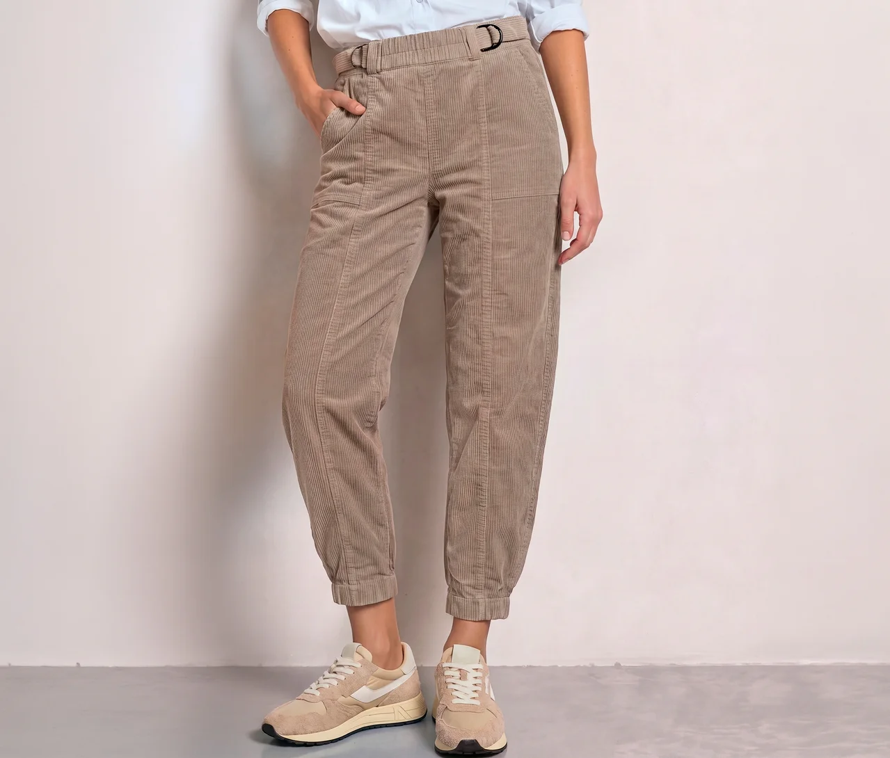 Personne portant un pantalon en velours côtelé Street One beige avec boucle en D et taille élastique, une main dans la poche, avec des baskets claires.