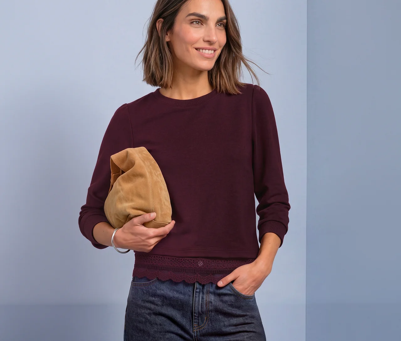 Une femme souriante aux cheveux bruns courts porte un T-shirt en jersey 3/4 Street One rouge avec une bordure en dentelle, un jean foncé et tient une pochette marron clair.