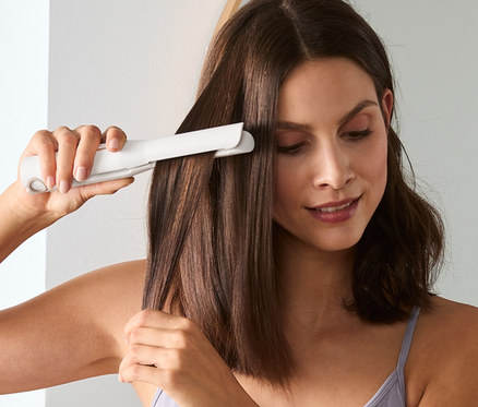 Femme se lisse les cheveux avec un fer à lisser sans fil.