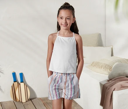 Une fille porte un 2 hauts en coton bio blanc et un short rayé.