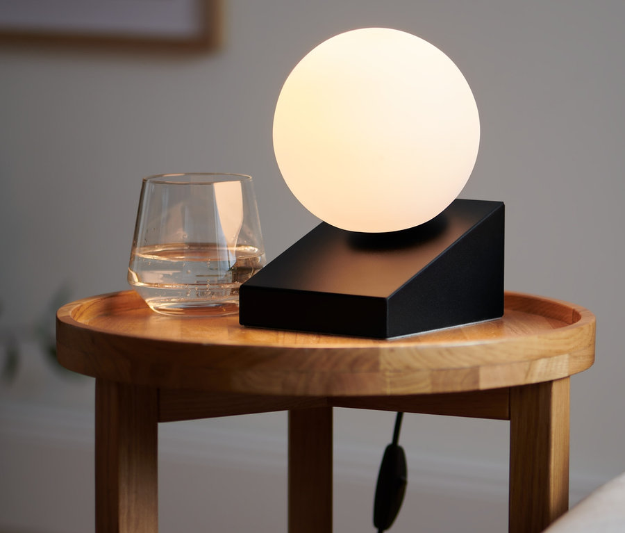 Sur une table en bois se trouve une lampe de table « globe en verre » à côté d'un verre d'eau.