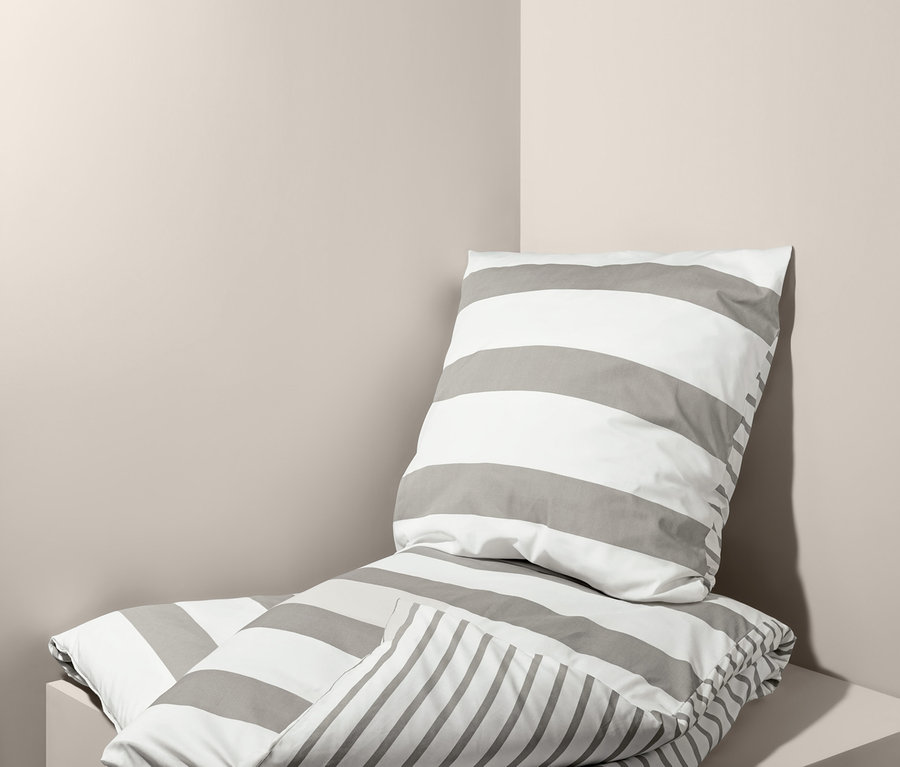Parure de lit en percale pliée avec des rayures grises, taille normale et taille double, posée l'une sur l'autre dans un coin.