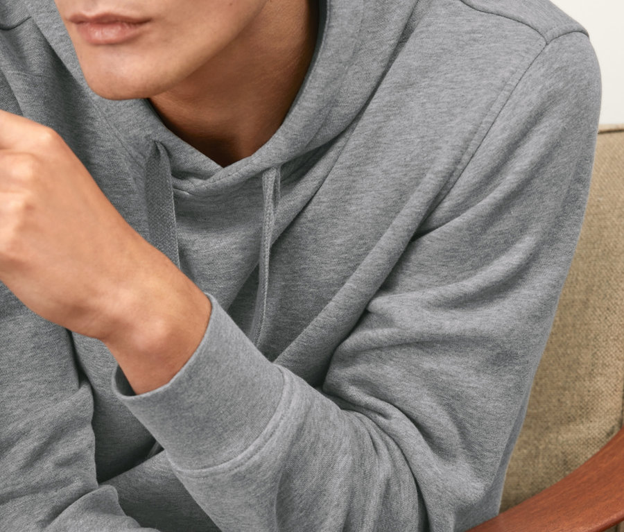 Un homme est assis dans un fauteuil et porte un sweat-shirt à capuche gris.