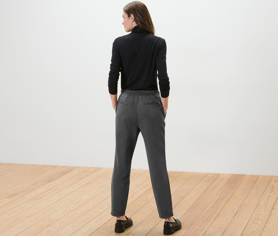 Une femme vue de dos porte un haut à manches longues noir et un pantalon de jogging gris.