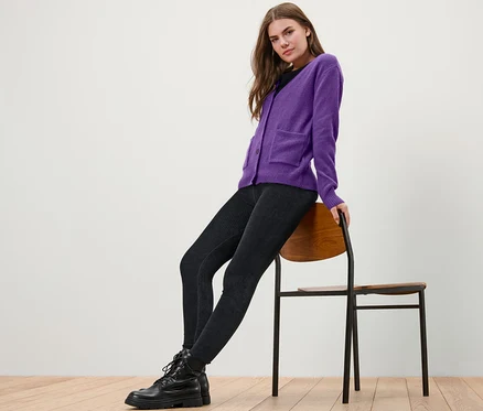Femme assise sur une chaise portant une jaquette en maille violette avec de la laine.