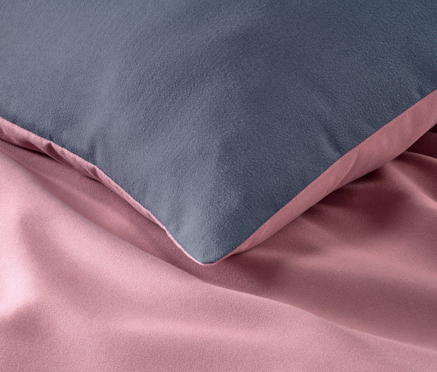 Gros plan d'un oreiller gris sur une parure de lit rose en microfibre et flanelle.