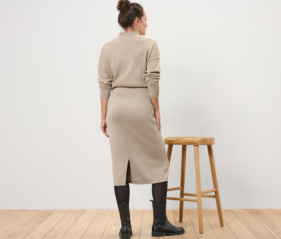 Une femme, vue de dos, porte une jupe tricotée, des collants et des bottes.