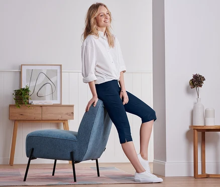 Femme assise de côté sur un fauteuil bleu, portant un pantalon capri bleu marine.