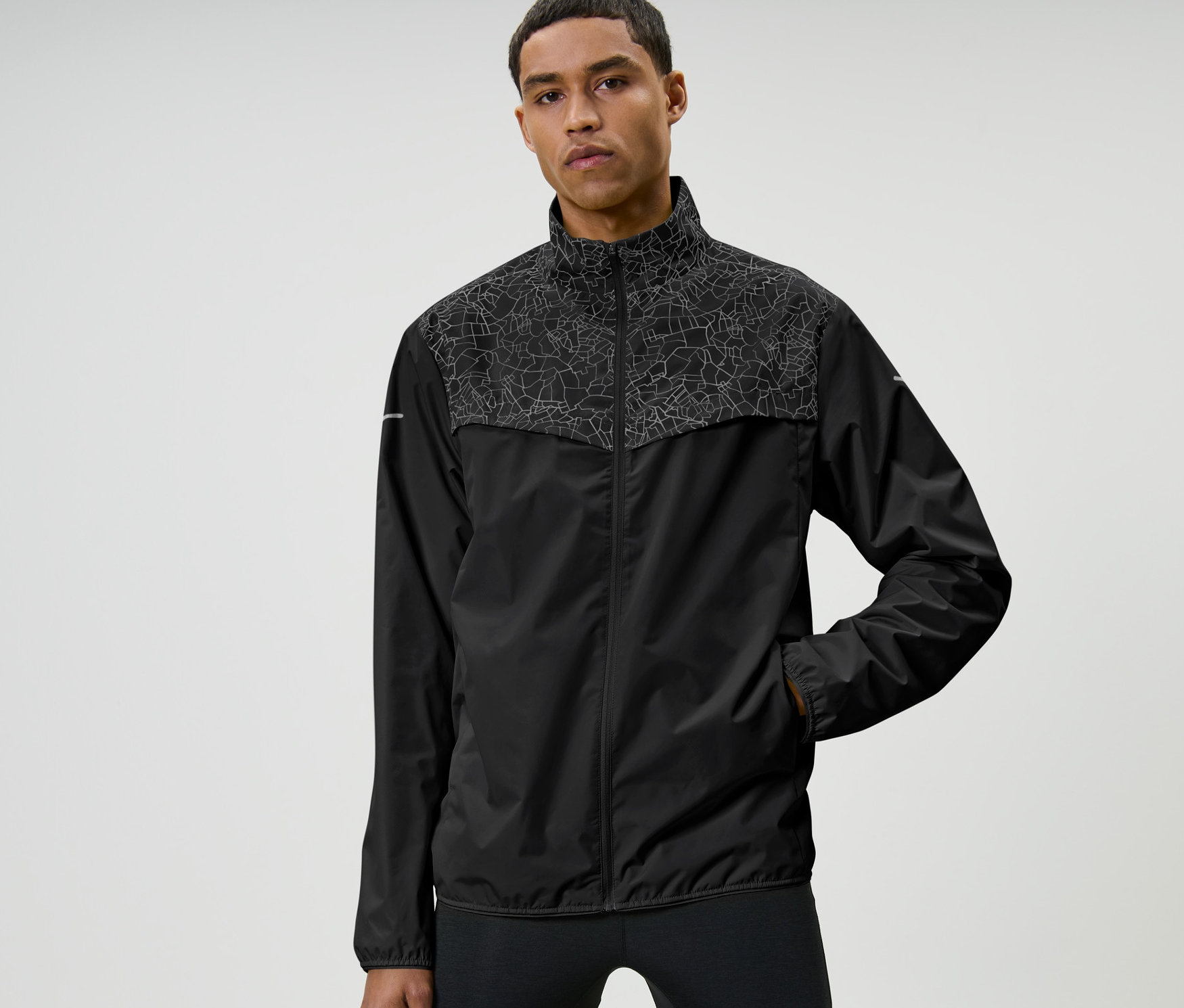 Un homme pose en veste de sport coupe-vent, noir.