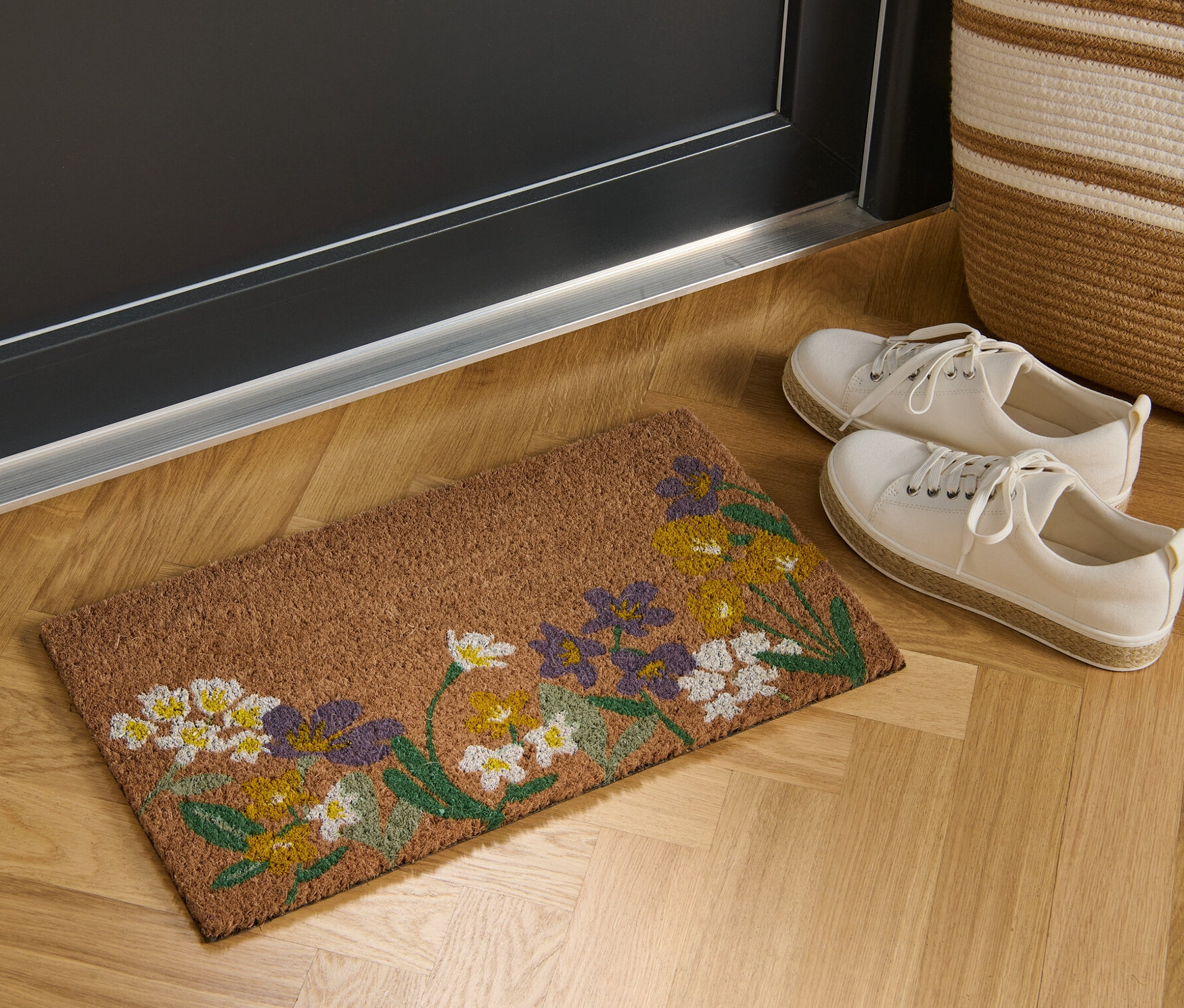 Un paillasson en fibre de noix de coco avec un motif floral est placé devant une porte.