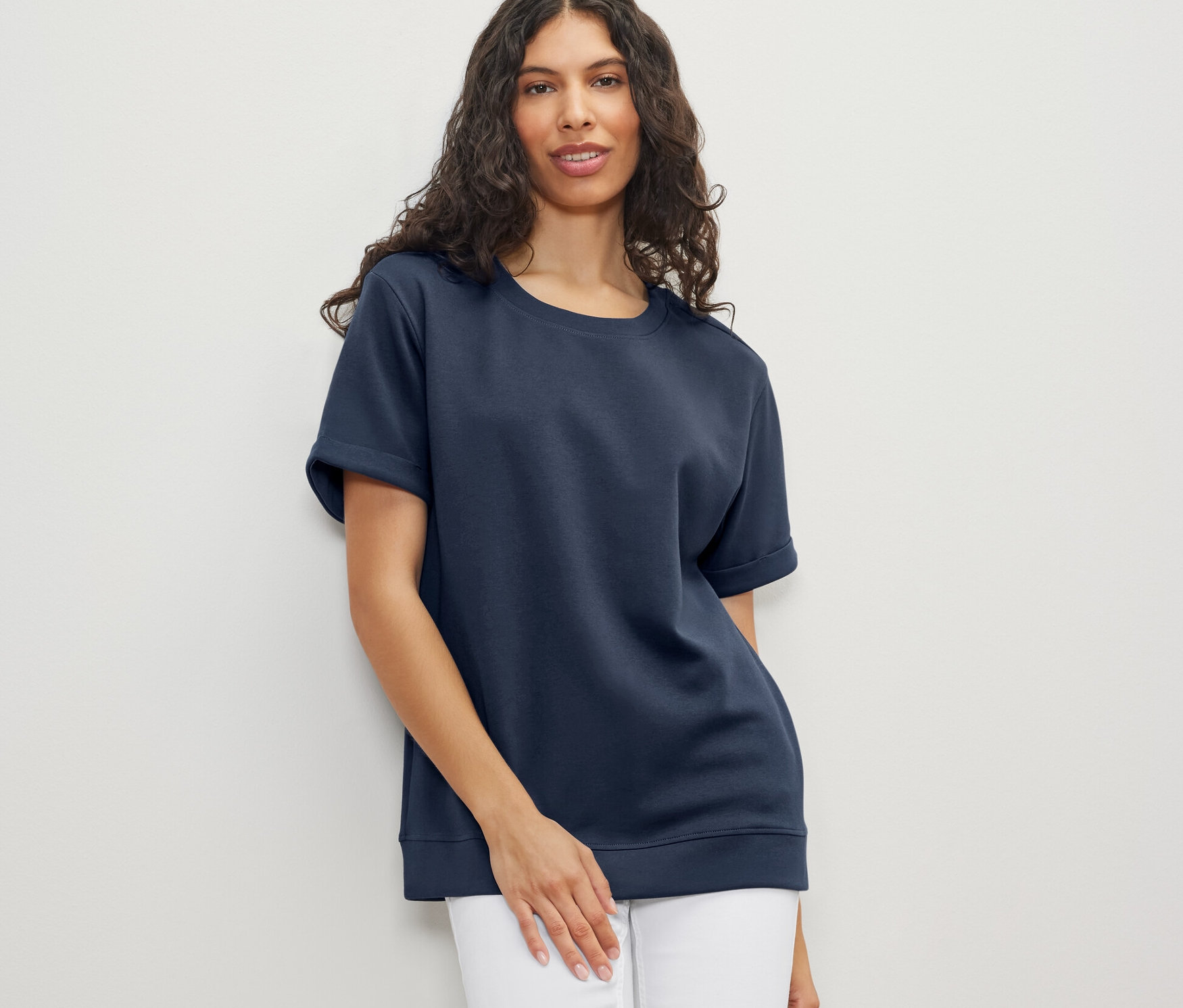 Une femme porte un t-shirt bleu foncé en mélange modal et un jean blanc.