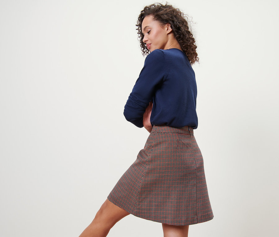 Femme posant en jupe tissée à carreaux et pull bleu.