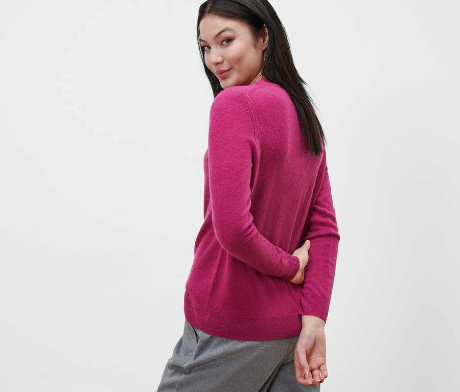 Femme regardant par-dessus son épaule et portant un pull en maille fine avec du cachemire, berry, et un pantalon gris.