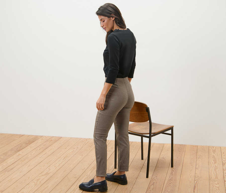 Une femme se tient de côté et porte un pantalon stretch avec jacquard pied-de-poule et un haut noir.