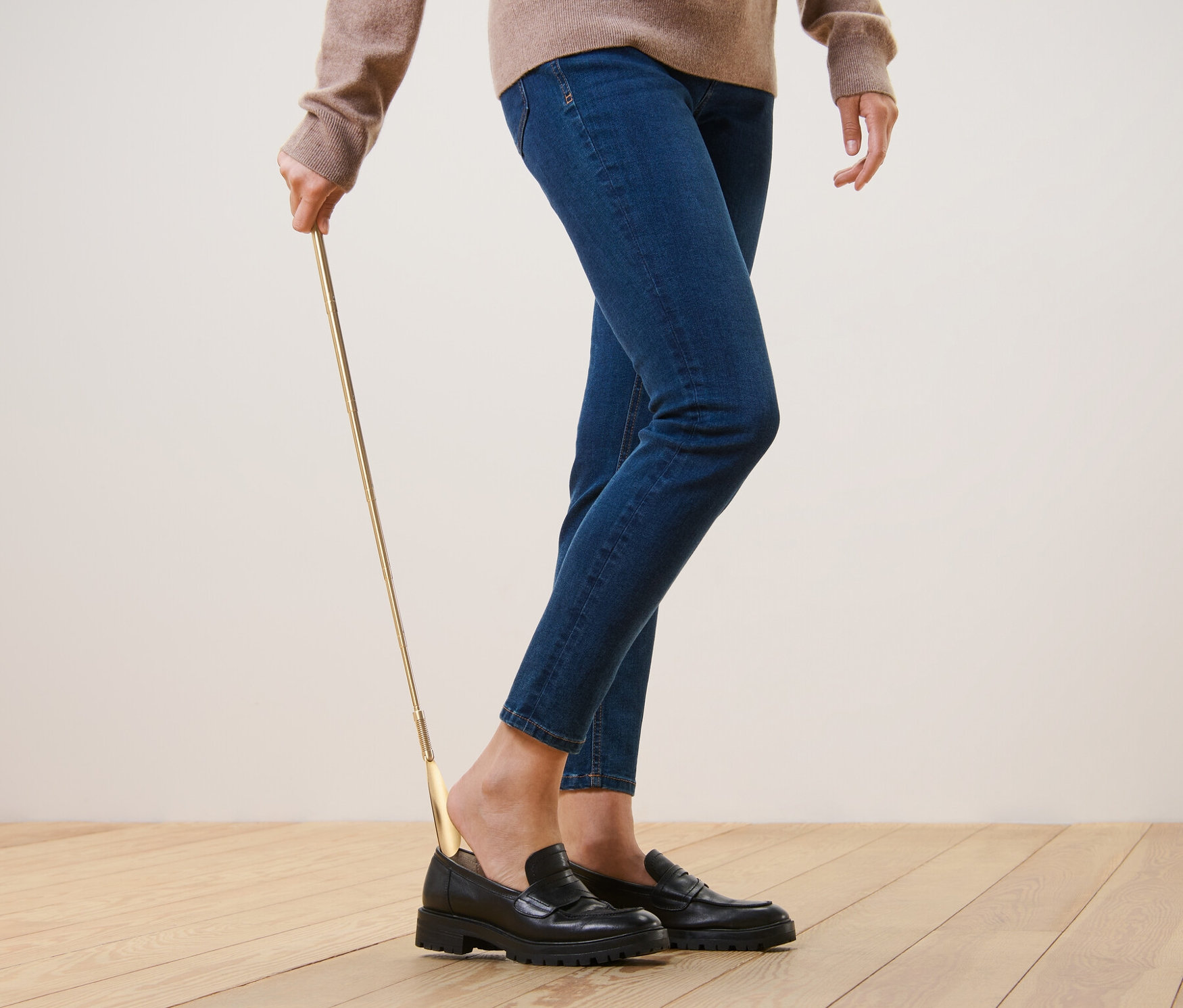 Une personne utilise un chausse-pied télescopique pour enfiler des chaussures noires.
