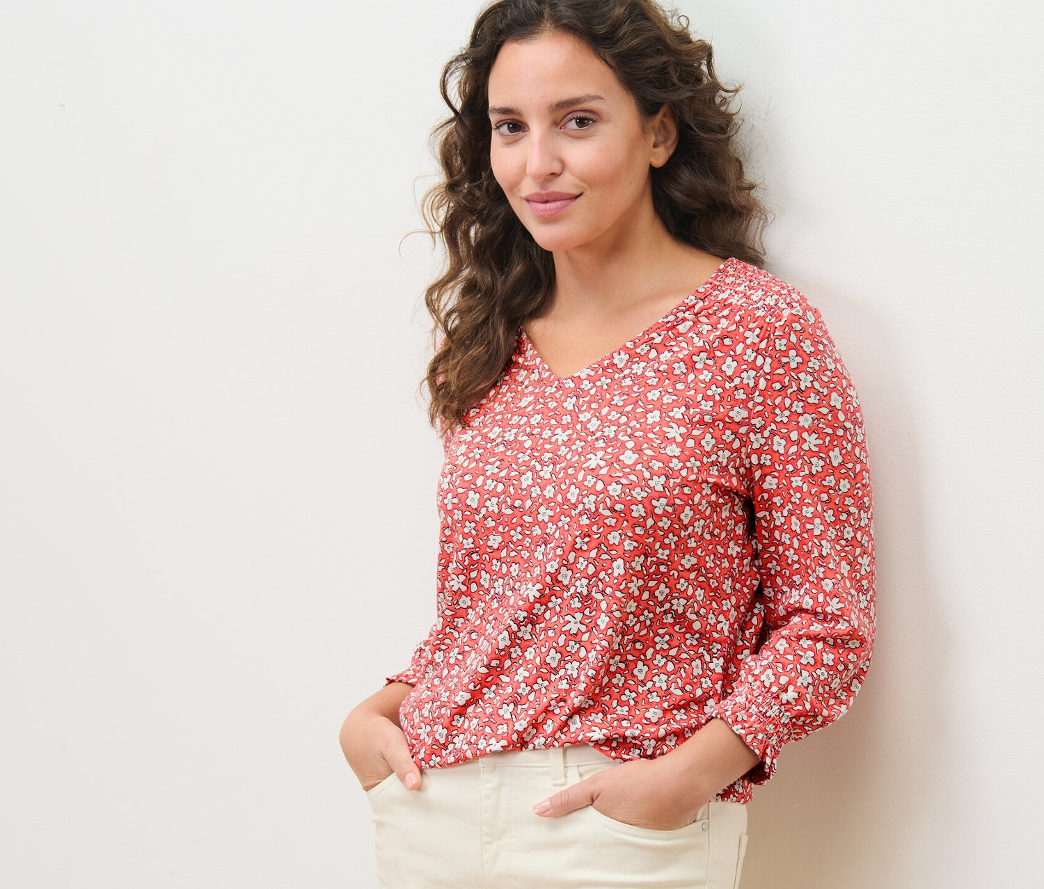 Femme posant dans une blouse imprimée corail et un pantalon clair.