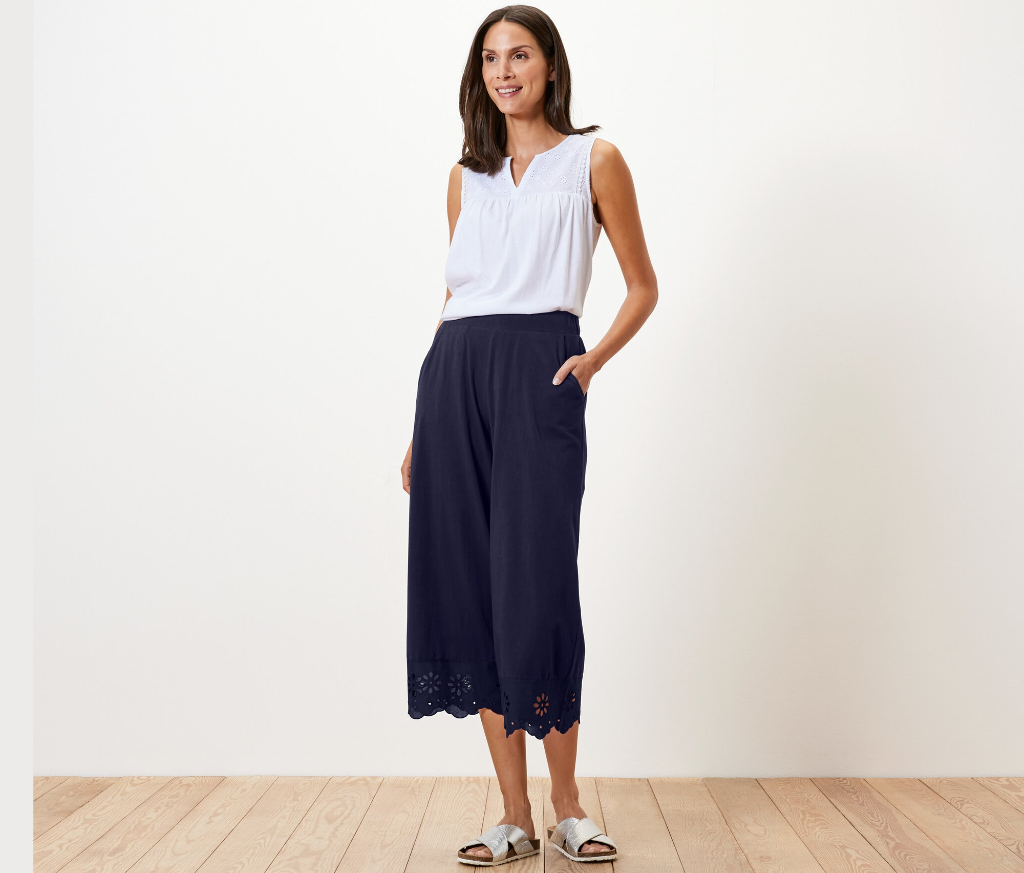 Une femme pose en haut blanc et culotte bleu marine avec broderie.