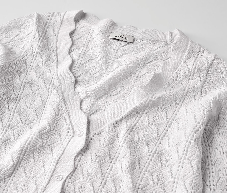 Gros plan sur une jaquette en maille blanche à motif ajouré.