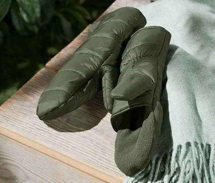 Une paire de mitaines-moufles surpiquées à côté d'une écharpe vert clair à franges sur une caisse en bois.
