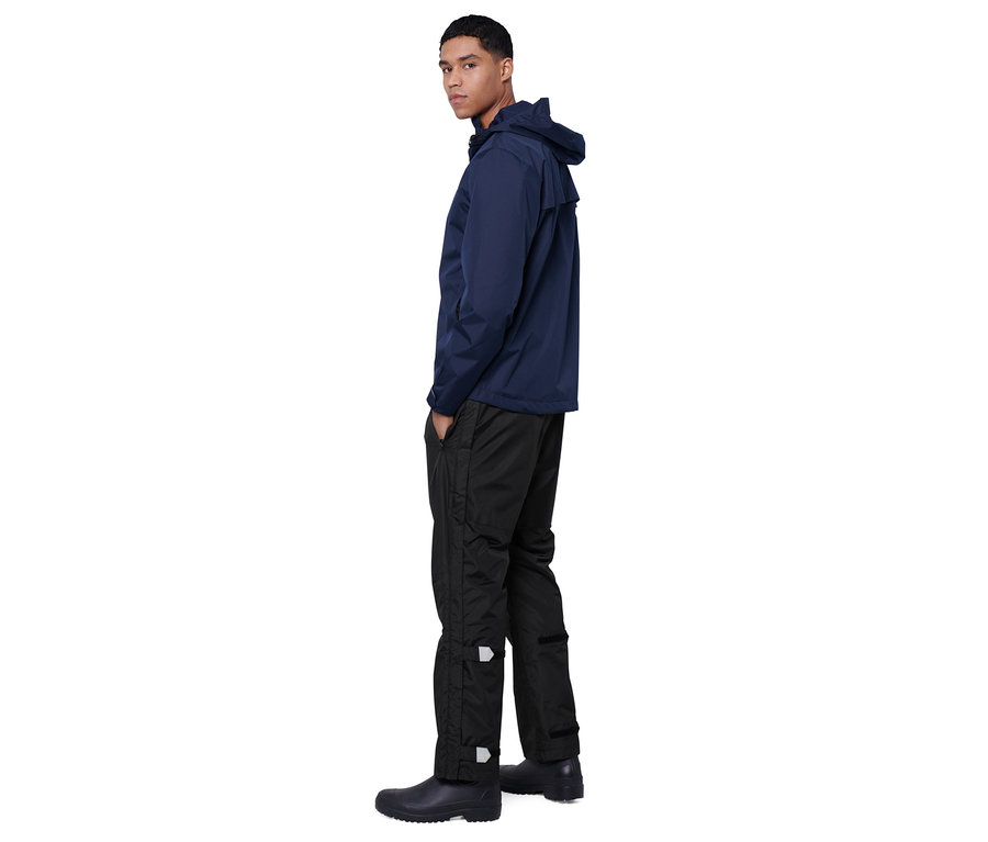 Un homme pose en veste de pluie high-tech bleue et pantalon de pluie high-tech noir.