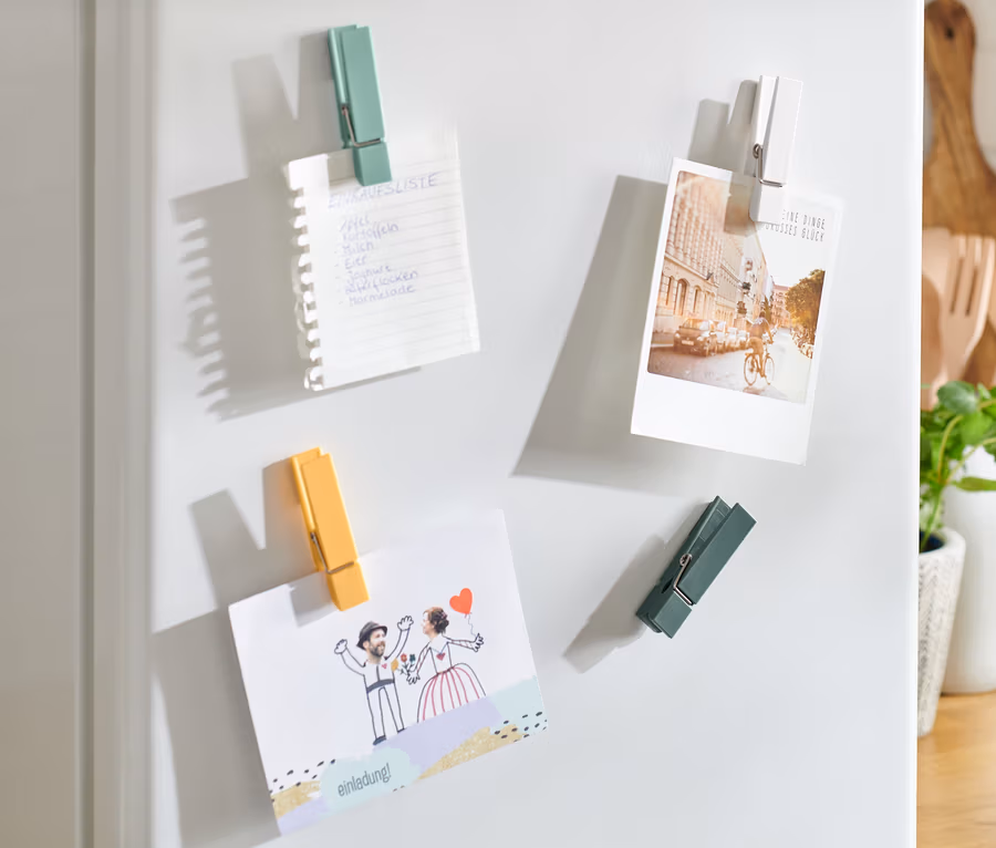 Un réfrigérateur blanc avec 4 aimants pour réfrigérateur tenant une liste de courses, une photo et une invitation de mariage.