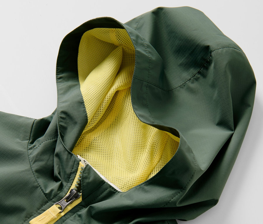 Gros plan sur une veste fonctionnelle de sport verte pour enfant avec une capuche et une fermeture éclair jaune.